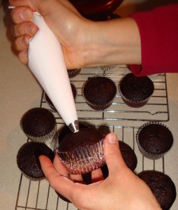 pastry bag with whipped topping getting squeezed into cupcake